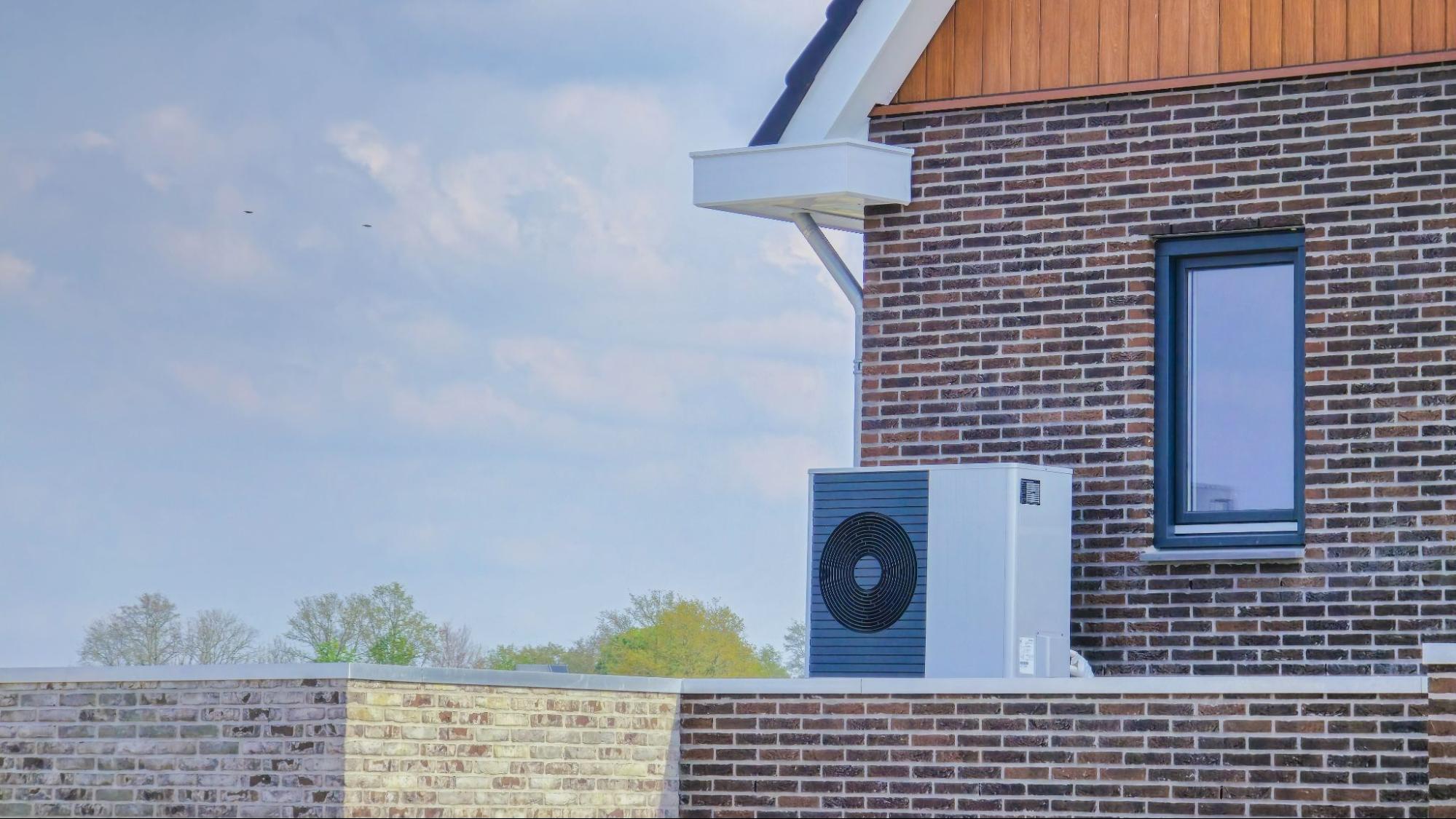 An air-source heat pump unit is installed outdoors at a modern brick home for efficient heating and cooling.