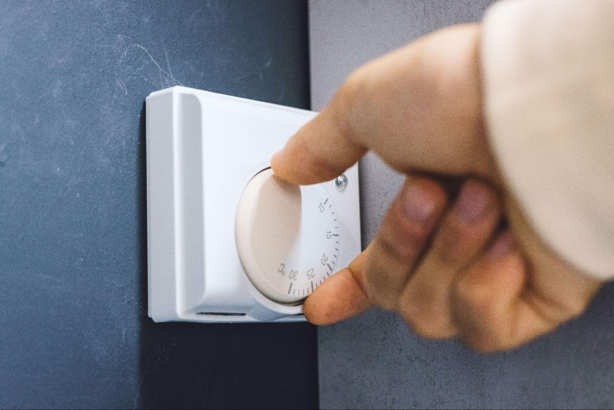 Close-up of a hand adjusting the temperature on a wall-mounted digital thermostat.