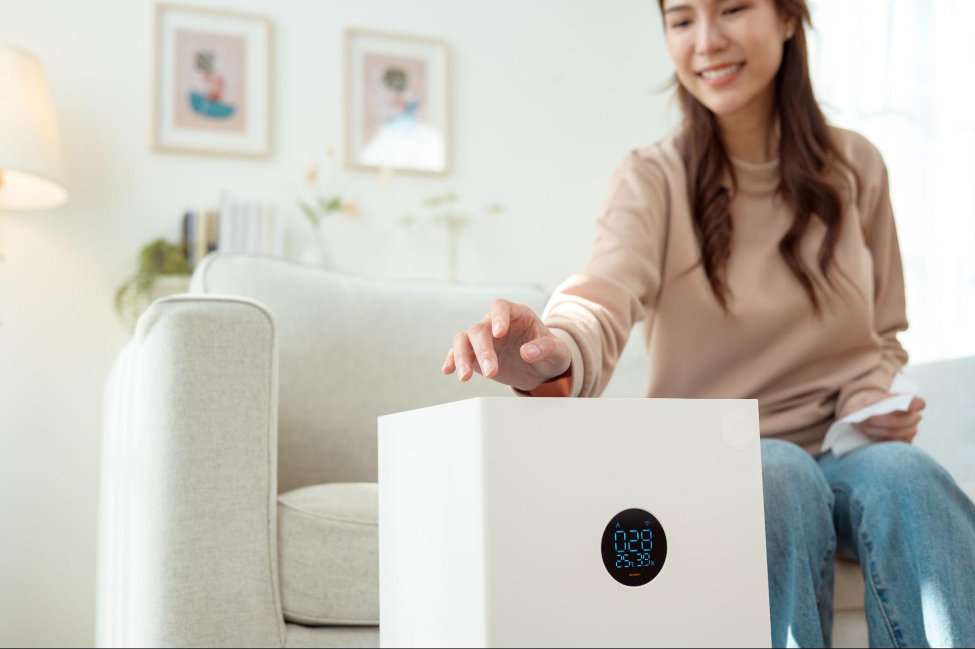 A woman turning on an air purification system in the living room of her home.
