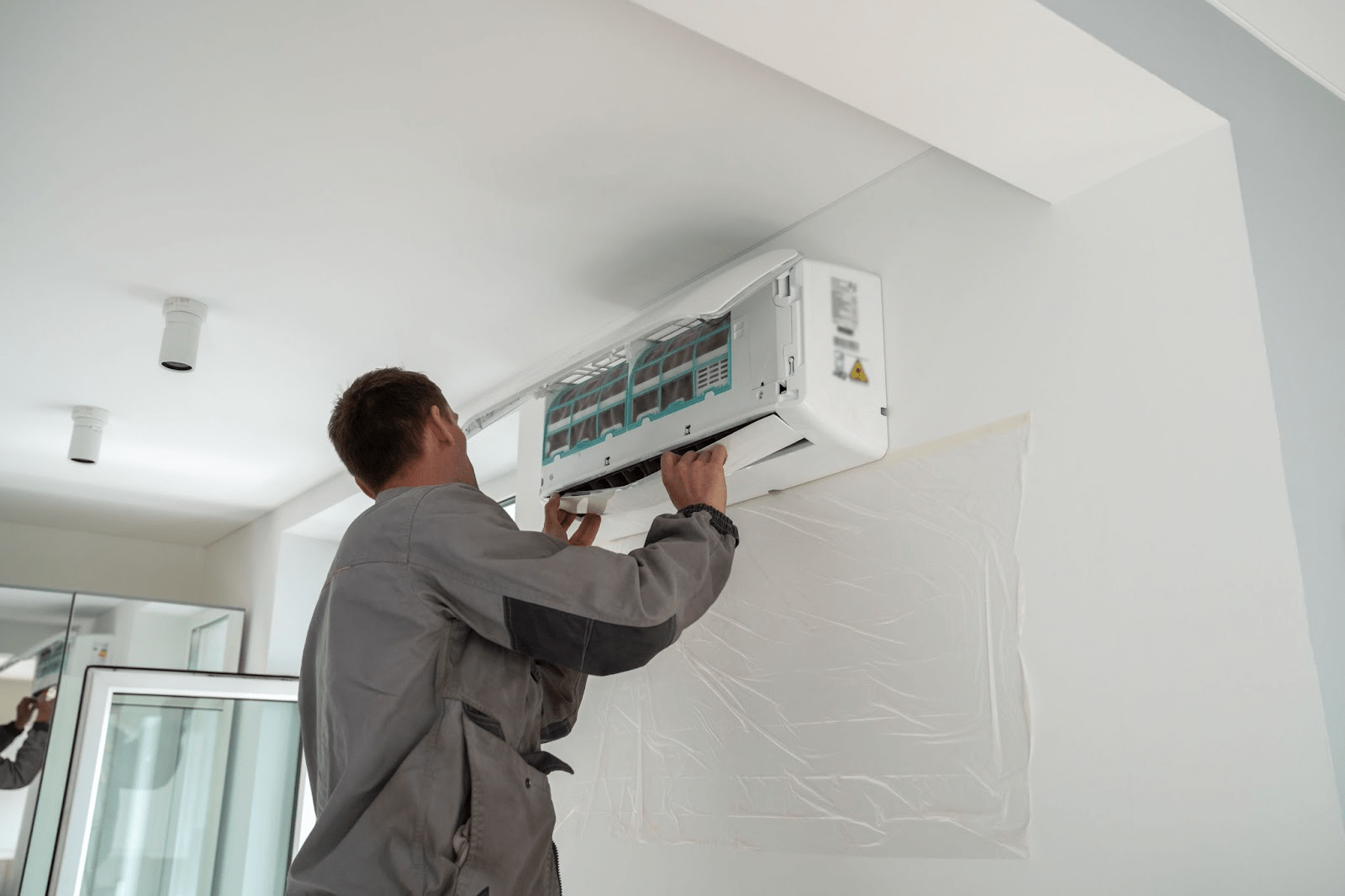 An HVAC technician mounts an air conditioning unit on an apartment wall.