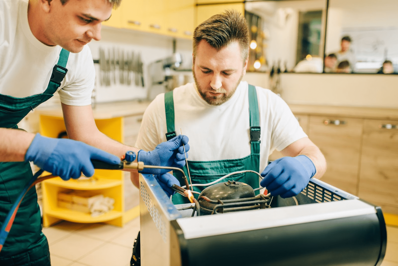 Two appliance technicians repair a refrigerator burner system at a residential unit.